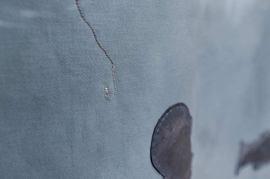 Detalhe do anzol bordado sobre tecido azul, obra O silêncio é quebrado, de Bia Távora